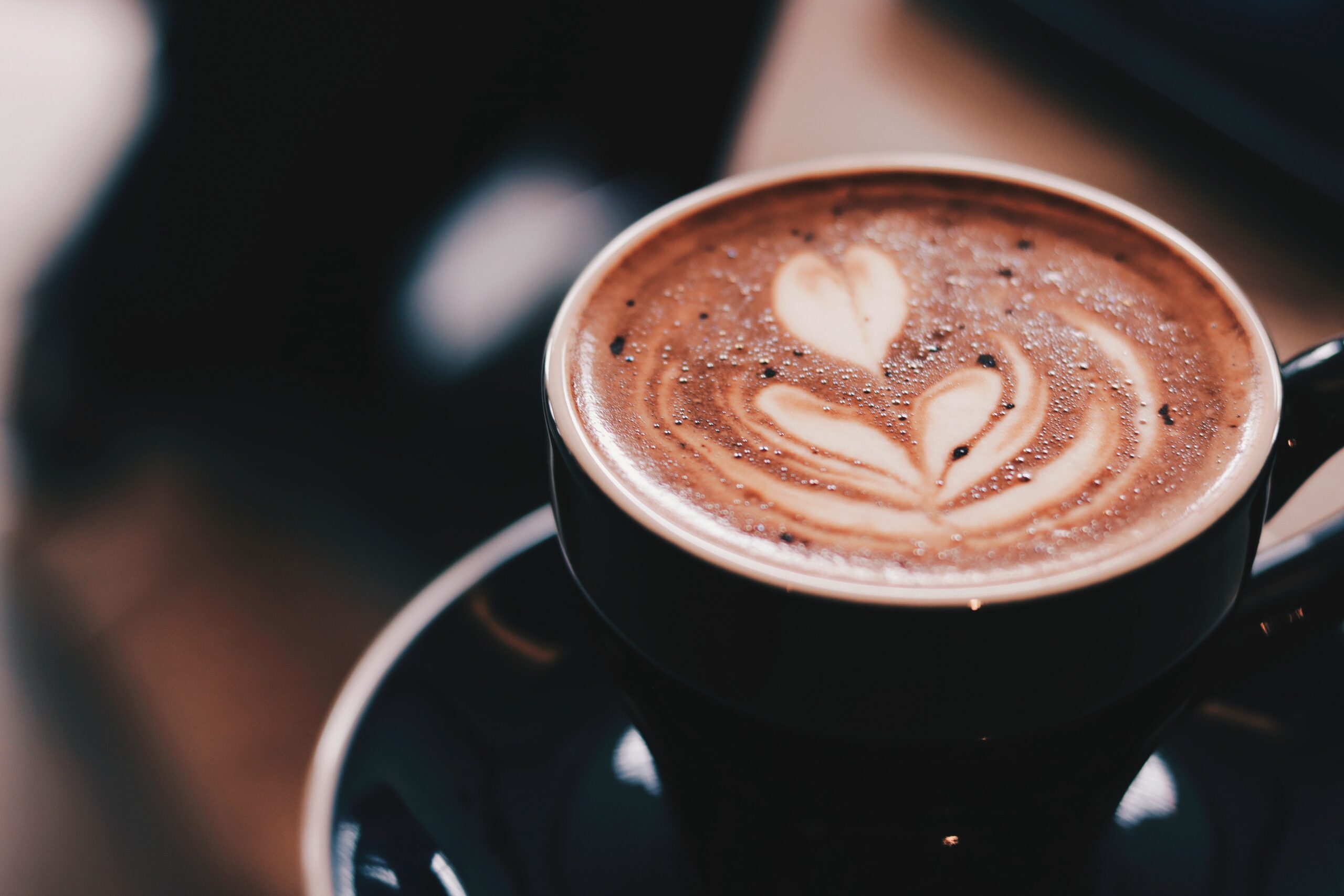 Fresh coffee dusted in chocolate in a black mug sitting on a saucer.